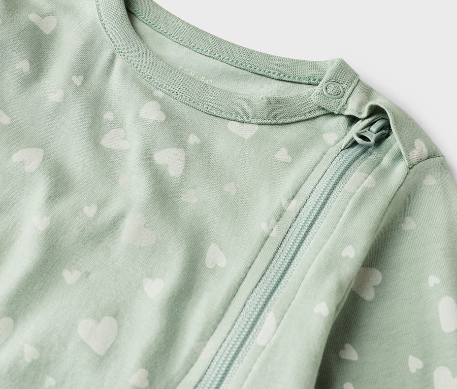 Detail záberu svetlozeleného detského overalu s bielym vzorom srdca a zipsom.