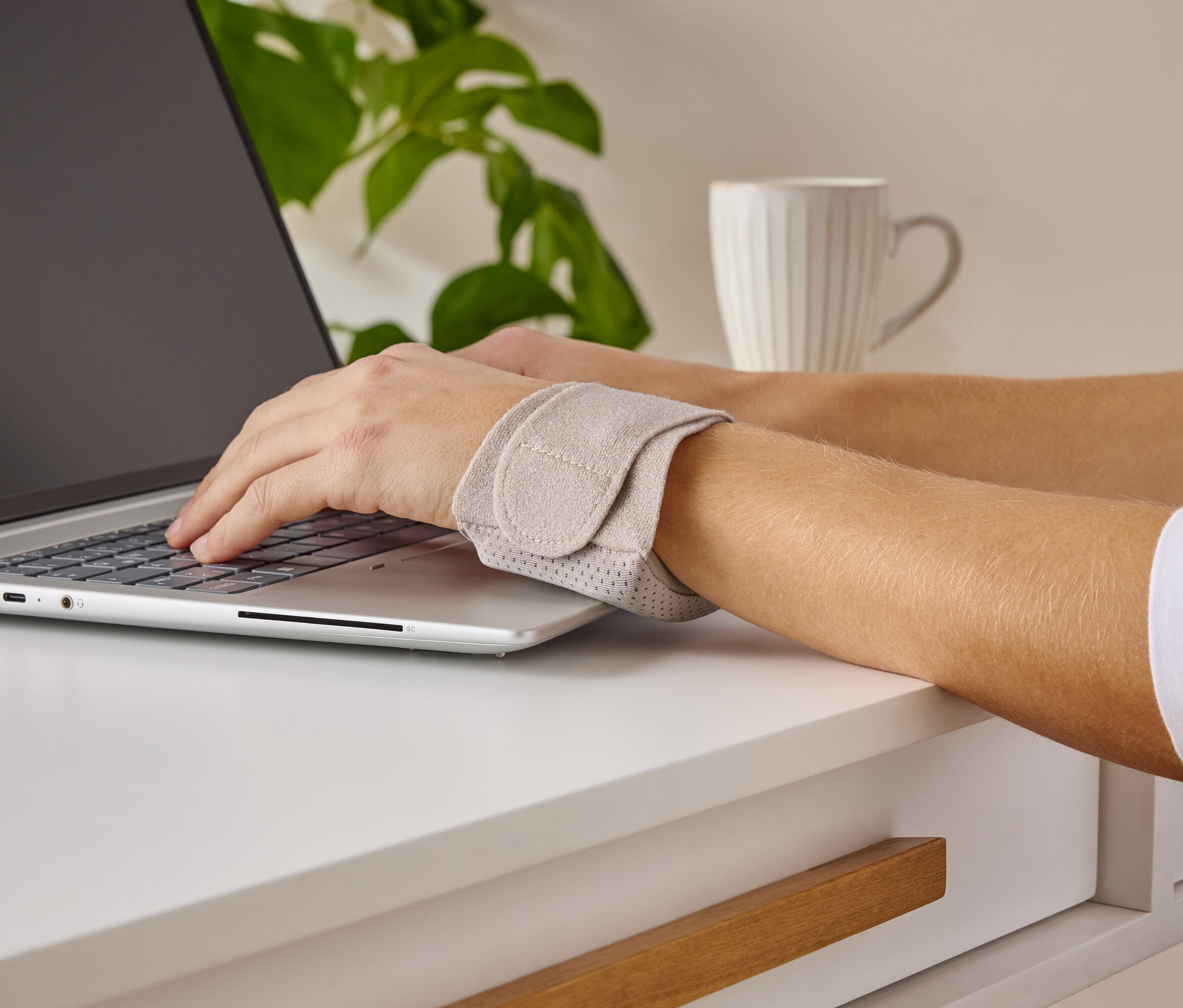 Osoba píše na notebooku a nosí podporu zápästia.