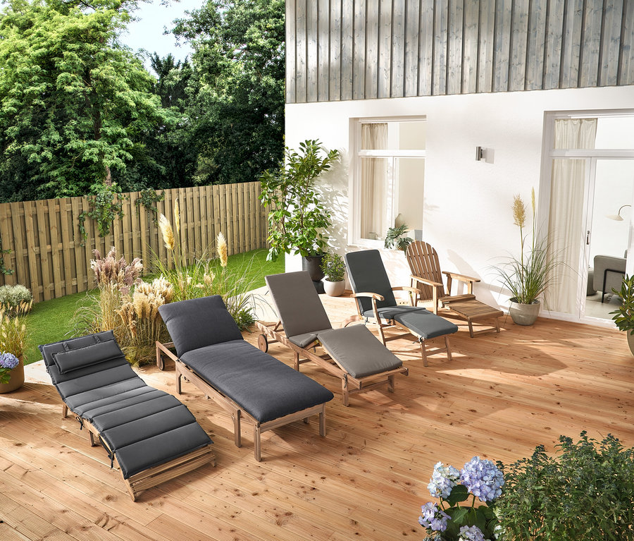 Na drevenej terase stojí niekoľko záhradných ležadiel a Adirondack relaxačné kreslo s vyťahovacou opierkou nôh z dreva.