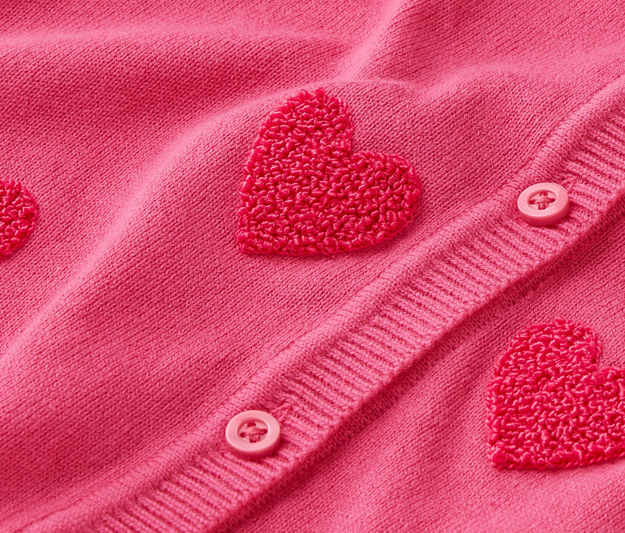 Detailný záber na ružový kardigán s aplikáciami v tvare srdca a gombíkmi.