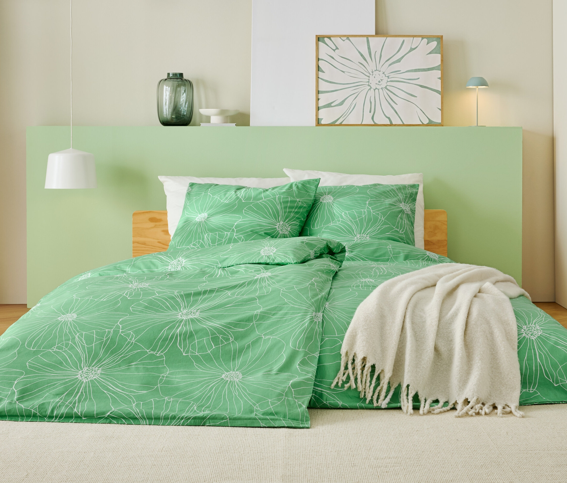 Posteľ so zelenou posteľnou bielizňou s bielym kvetinovým vzorom, bielou prikrývkou a svetlozeleným čelom.