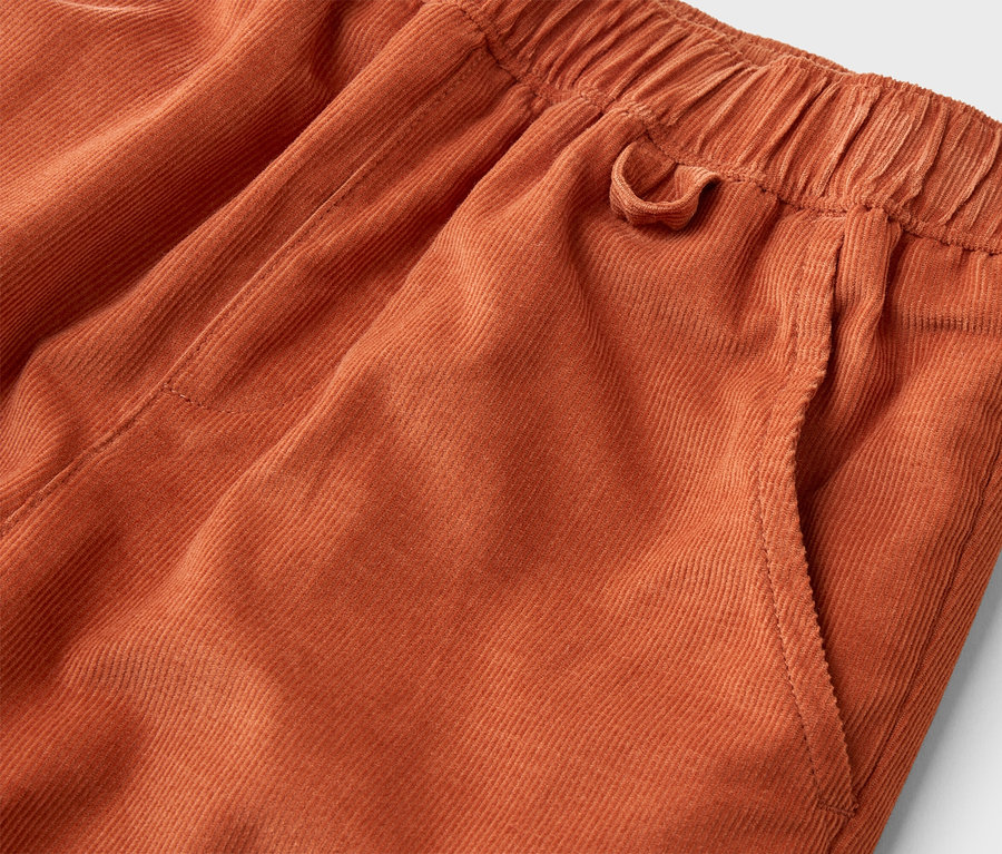 Detail oranžových menčestrových nohavíc s elastickým pásom a bočným vreckom.