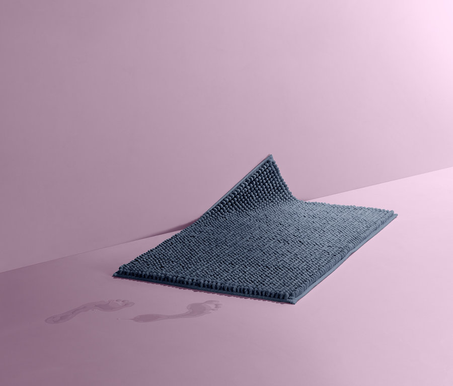 Modrá predložka do kúpeľne, cca 50 x 80 cm na ružovom pozadí. Na podlahe sú vidieť mokré stopy.