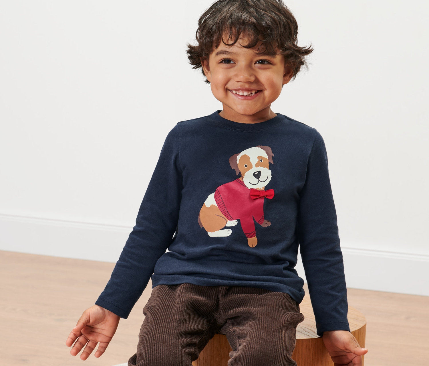 Chlapec sedí a má na sebe detské tričko s dlhými rukávmi s obrázkom psa.