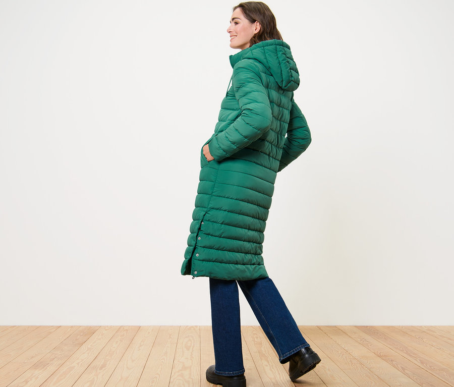 Žena pózuje bokom v dlhom prešívanom kabáte s kapucňou.