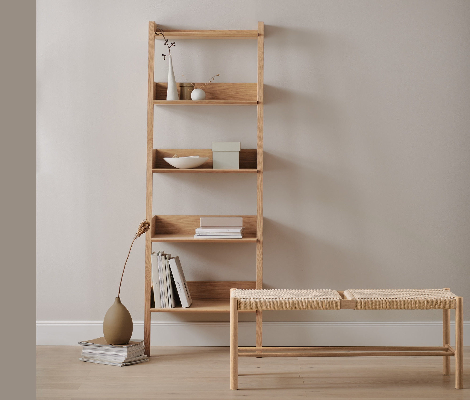 Dubový rebríkový regál s dekoráciami a knihami vedľa prútenej lavice.