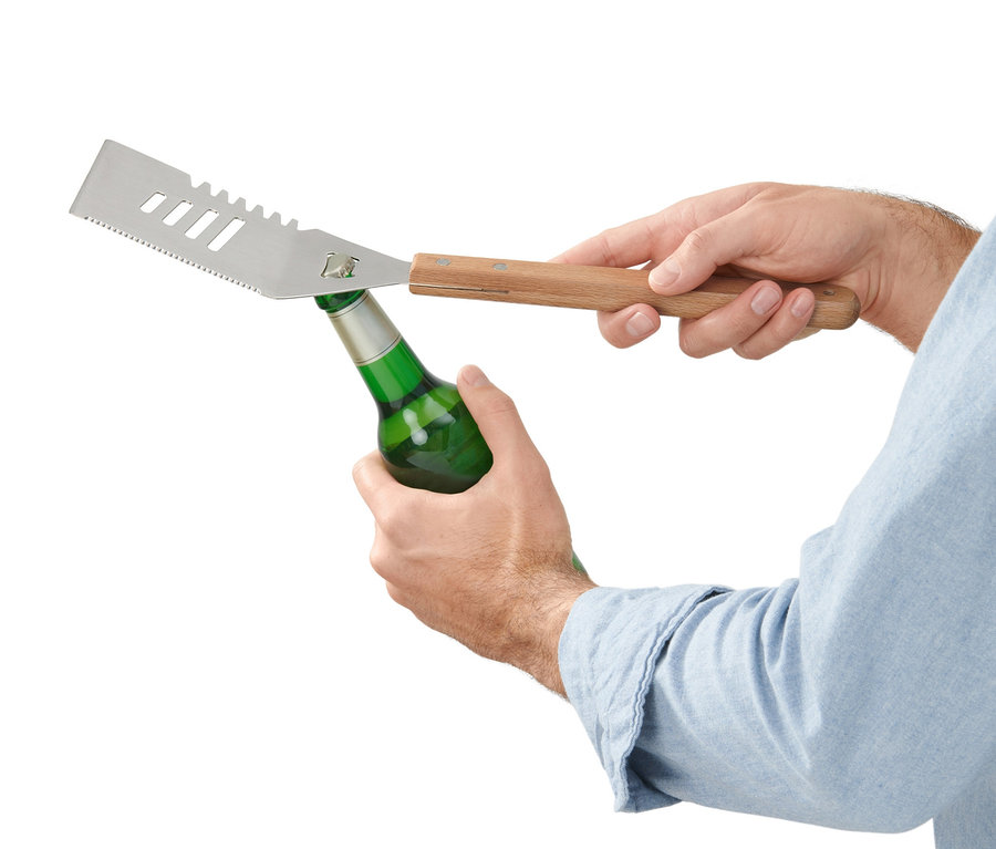 Muž otvára zelenú fľašu multifunkčným nástrojom na grilovanie.