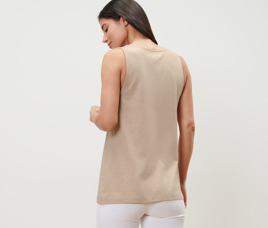 Žena chrbtom k fotoaparátu má na sebe béžový melírovaný top s gombíkovou légou a biele nohavice.