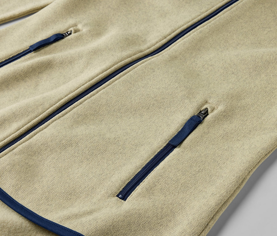 Detail žltej bundy z pleteného flaušu s modrými zipsami.