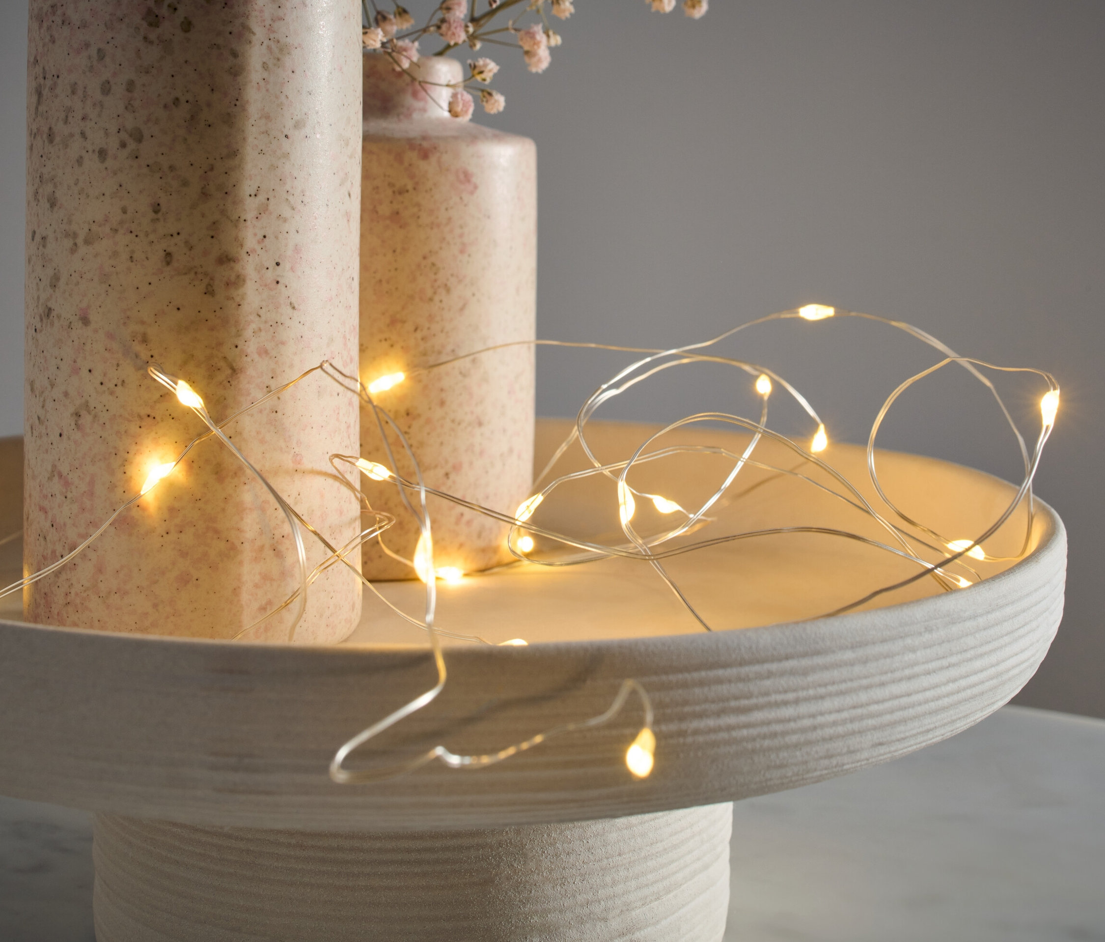 Svetelná reťaz s mikro LED, kvapky, leží na dekoratívnom podnose vedľa dvoch váz.