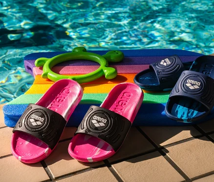 Dva páry arena Kinder-Badesandalen Junior Urban Active, pink a navy, ležia na farebnej plaveckej doske pri bazéne.