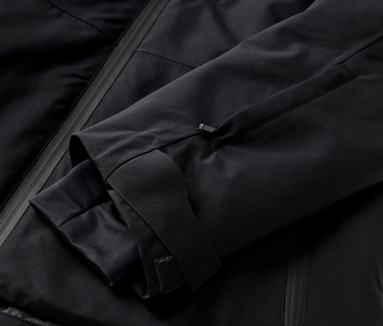 Detail čiernej bundy s rukávom a vreckom na zips.
