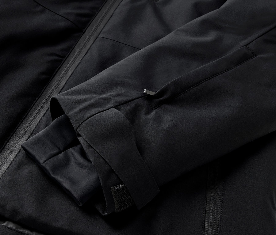 Detail čiernej bundy s rukávom a vreckom na zips.