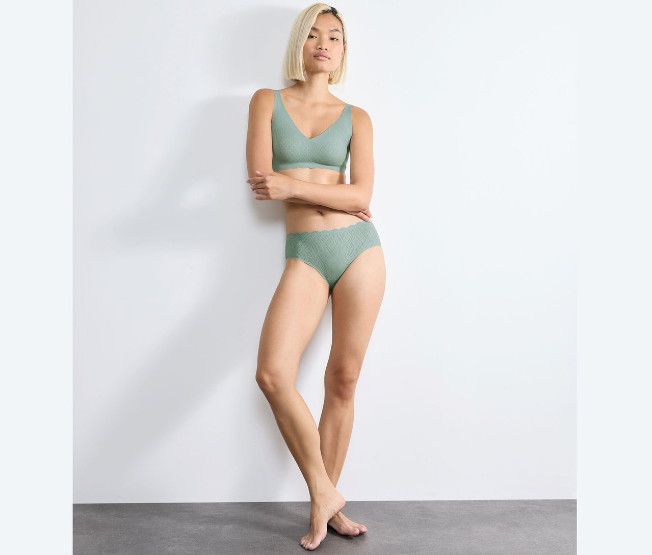 Žena pózuje v mäkkej podprsenke sloggi ZERO Feel Bliss Soft Bra, misty turquoise a zodpovedajúcich nohavičkách.