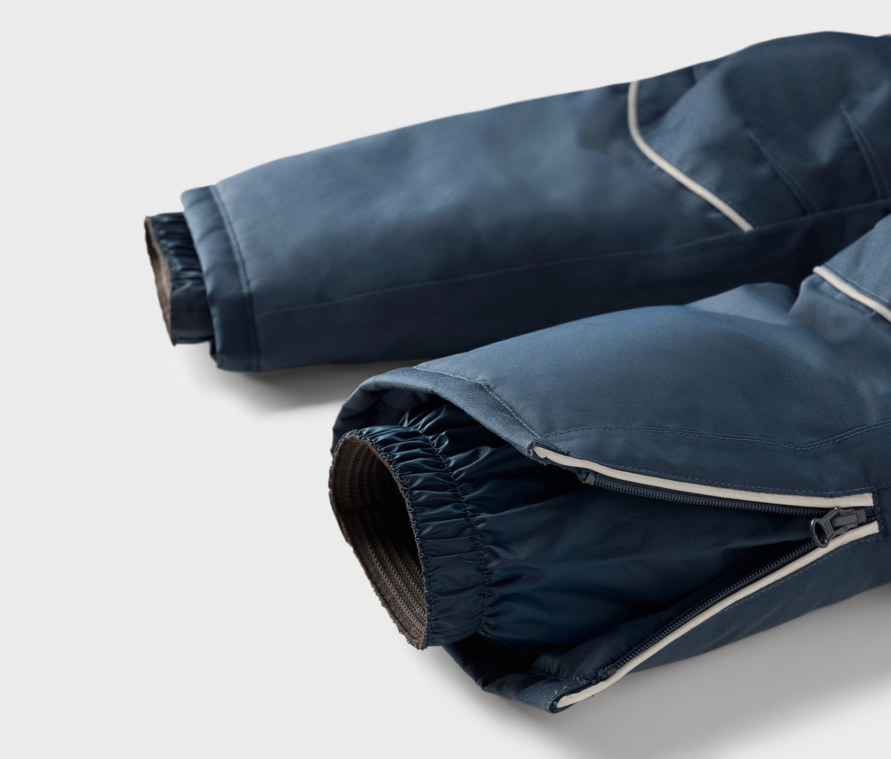 Detail modrých lyžiarskych nohavíc so zipsom na nohavici a reflexným prúžkom.