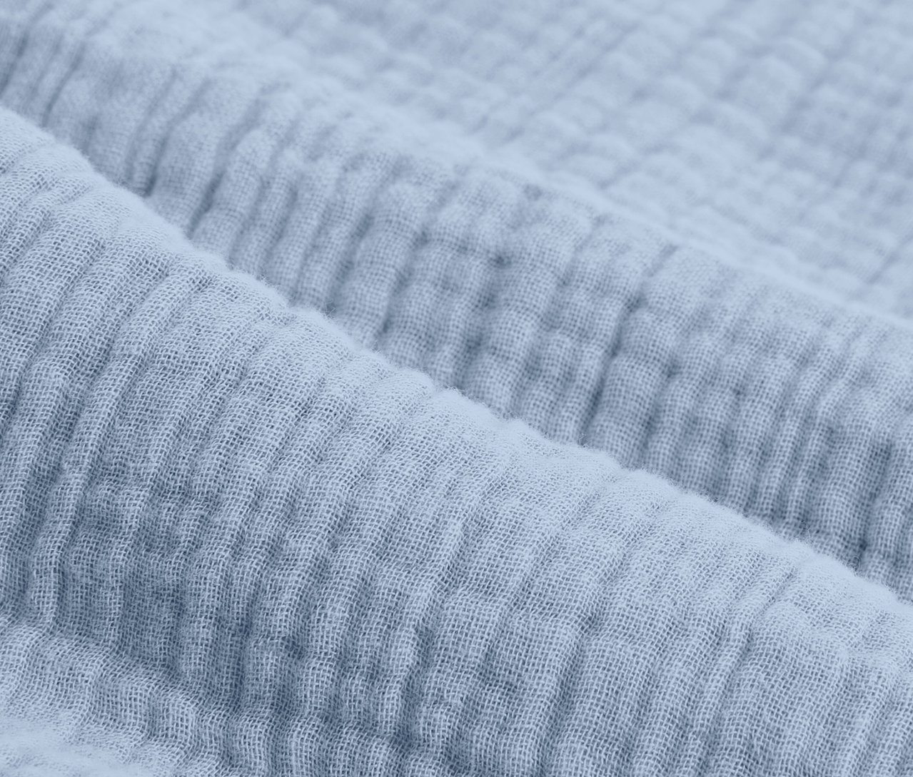 Detailný záber na svetlomodrú mušelínovú posteľnú bielizeň štandardnej veľkosti.