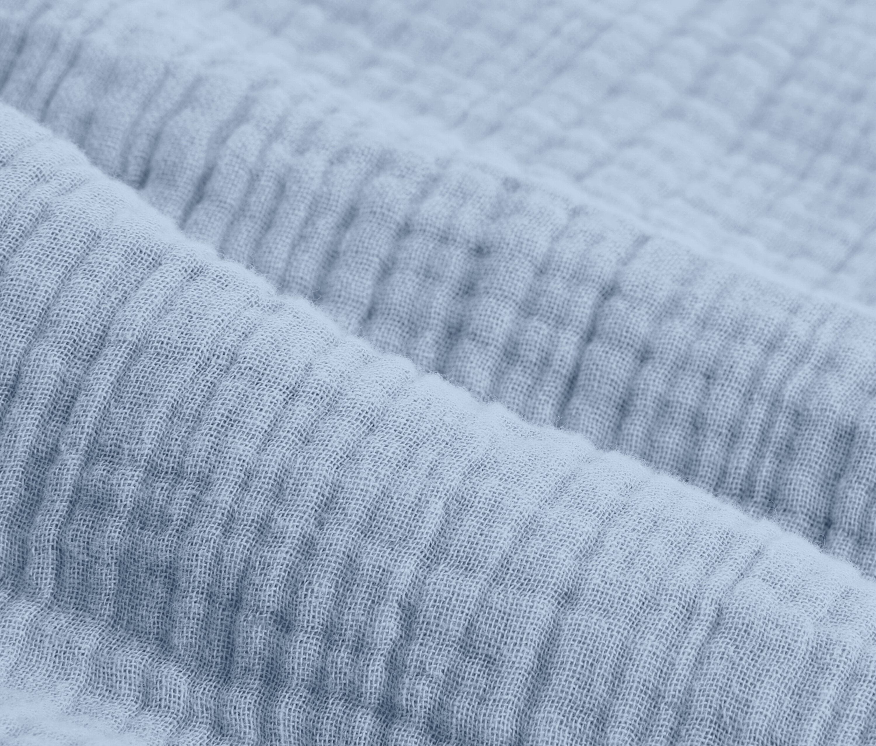 Detailný záber na svetlomodrú mušelínovú posteľnú bielizeň štandardnej veľkosti.