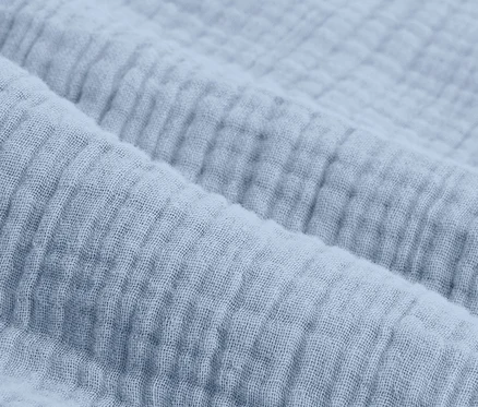 Detailný záber na svetlomodrú mušelínovú posteľnú bielizeň štandardnej veľkosti.