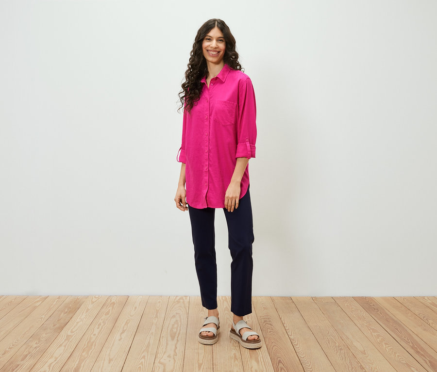 Žena stojí a má na sebe dlhú ľanovú blúzku ružovej farby.