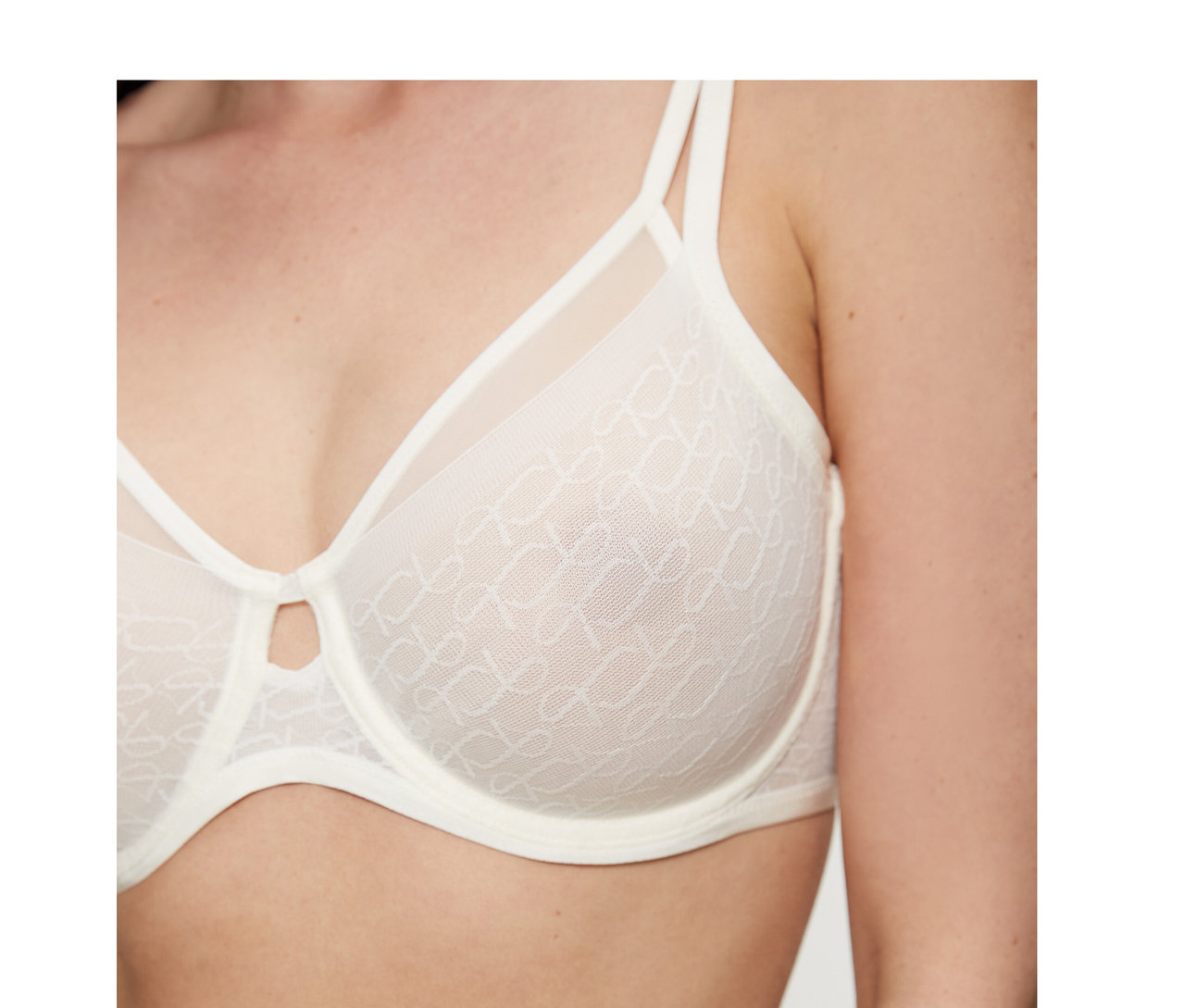 Žena má na sebe krémovobielu podprsenku Triumph Signature Sheer Minimizer so vzorovanými priesvitnými košíčkami a malým výrezom v strede.