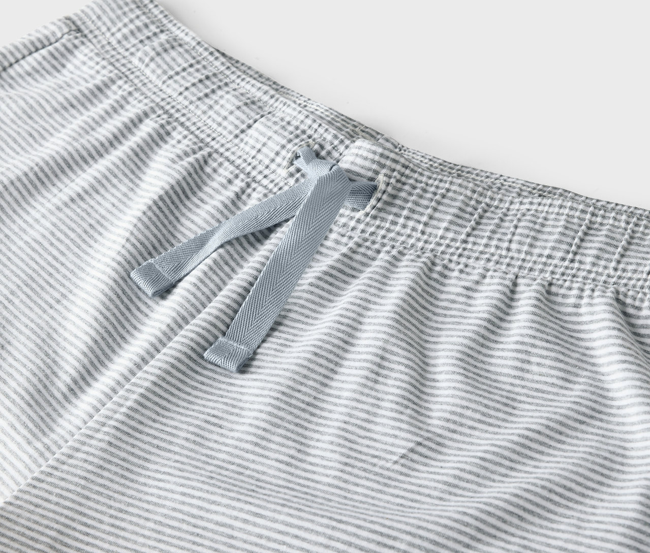 Detail sivo-bielych pruhovaných nohavíc s modrou sťahovacou šnúrkou v páse.