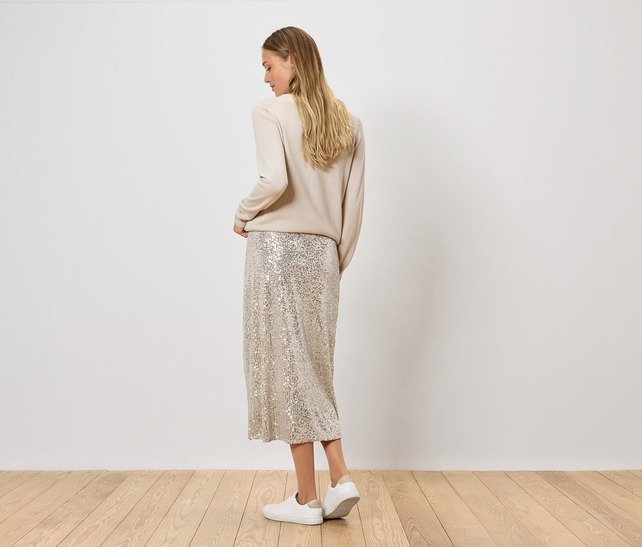 Žena pózuje v béžovom svetri a flitrovanej sukni so striebornými topánkami.