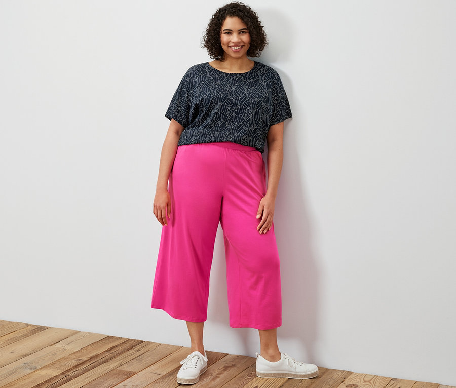 Žena stojí a má na sebe tmavomodré tričko s krátkym rukávom a džersejové nohavice culotte ružovej farby.