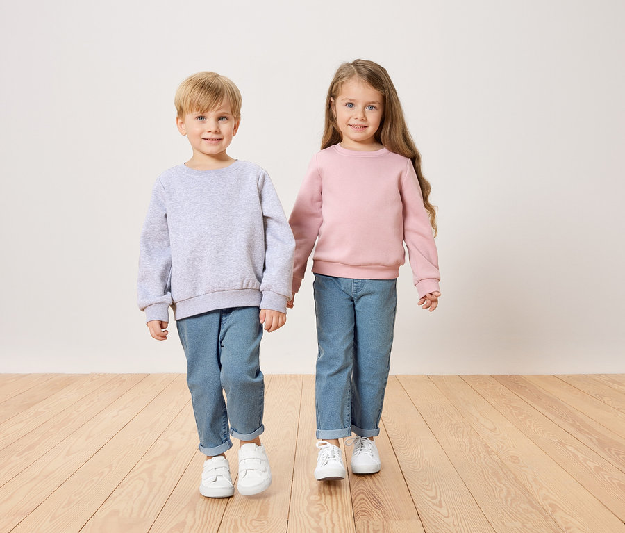 Chlapec v sivom svetri a dievča v ružovom svetri sa držia za ruky.