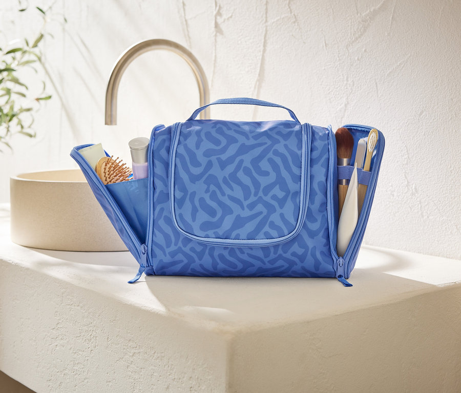 Otvorená, modrá kozmetická taška s abstraktným vzorom stojí na bielej doske v kúpeľni.