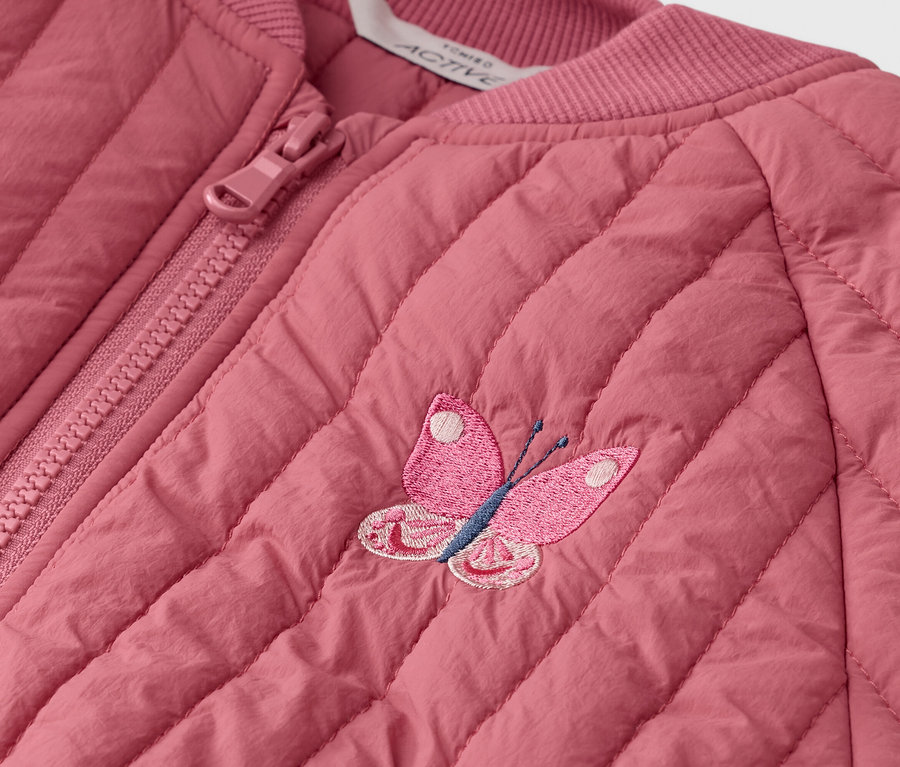 Detail záberu prešívanej ružovej bundy so zipsom a vyšívanou aplikáciou motýľa.