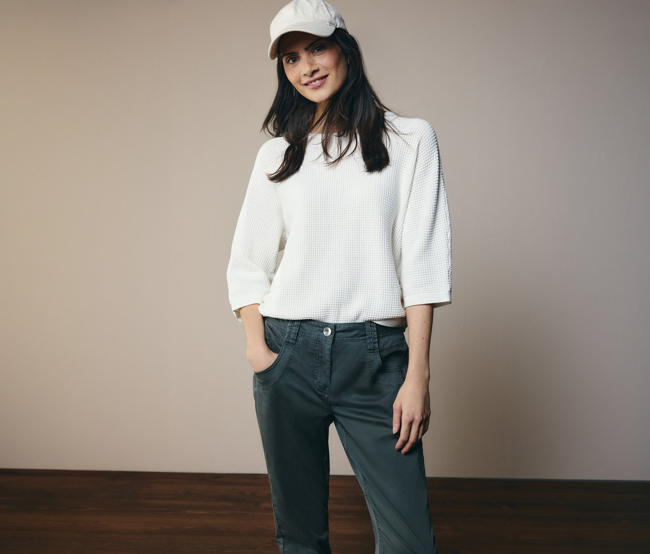 Žena v bielom tope a šiltovke pózuje v nohaviciach CECIL »Scarlett« s rukami vo vreckách.