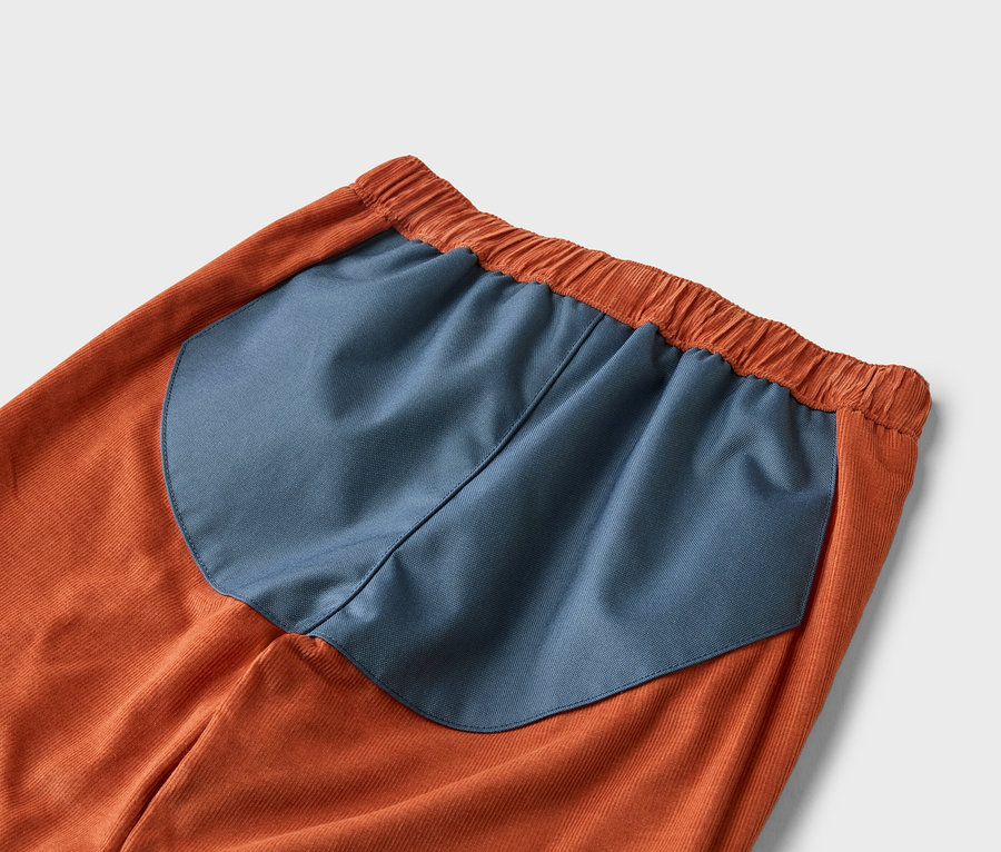 Detail oranžových menčestrových nohavíc s tmavomodrou vsadkou v páse.