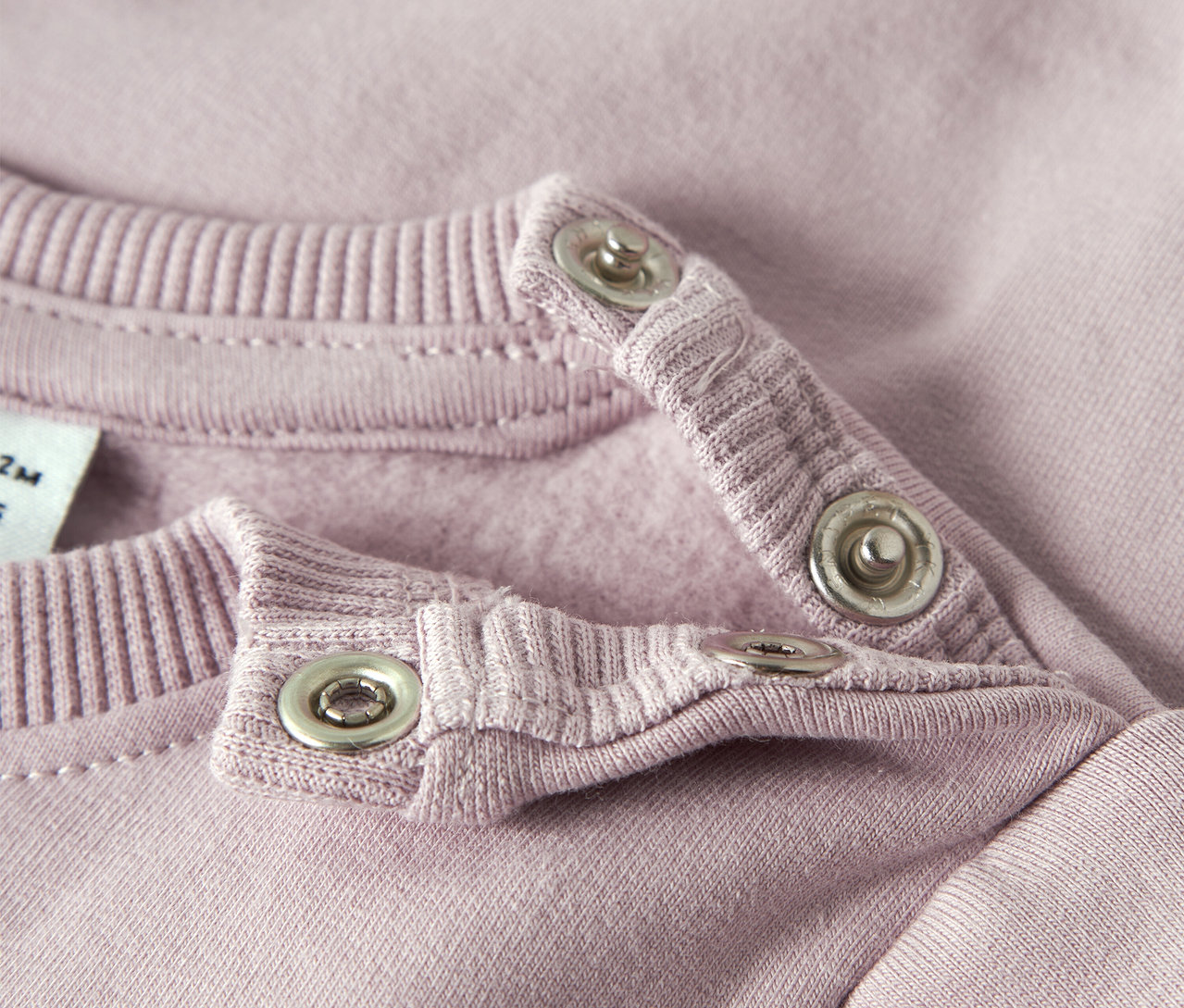 Detail ružovej dojčenskej mikiny NAME IT s patentkami na golieri.