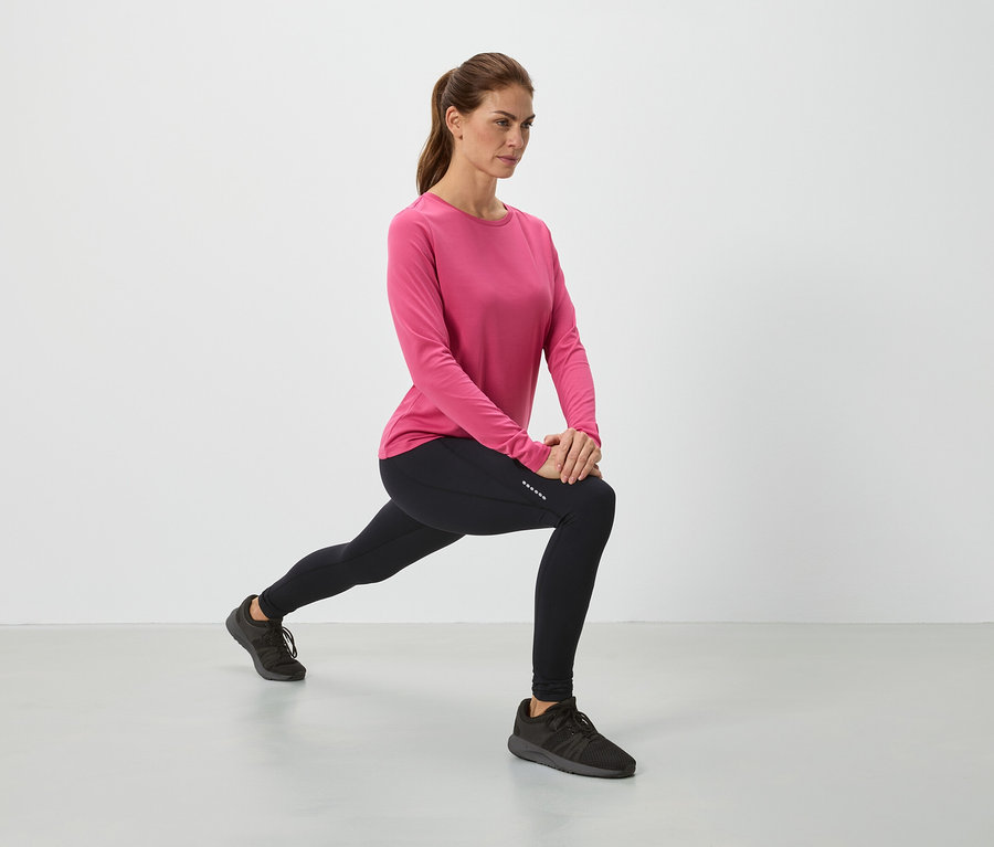 Žena v ružovom tope a čiernych legínach sa pretahuje.