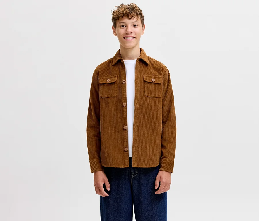 Usmiaty mladý muž v hnedej menčestrovej košeli Jack&Jones Regent, bielom tričku a modrých džínsoch.