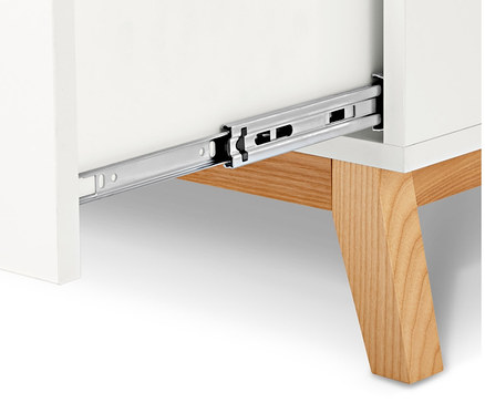 Detail bielej komody s otvorenou zásuvkou a drevenými nohami.