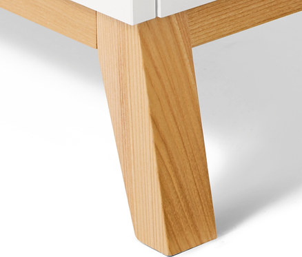 Detail bielej komody s nohami zo svetlého dreva.