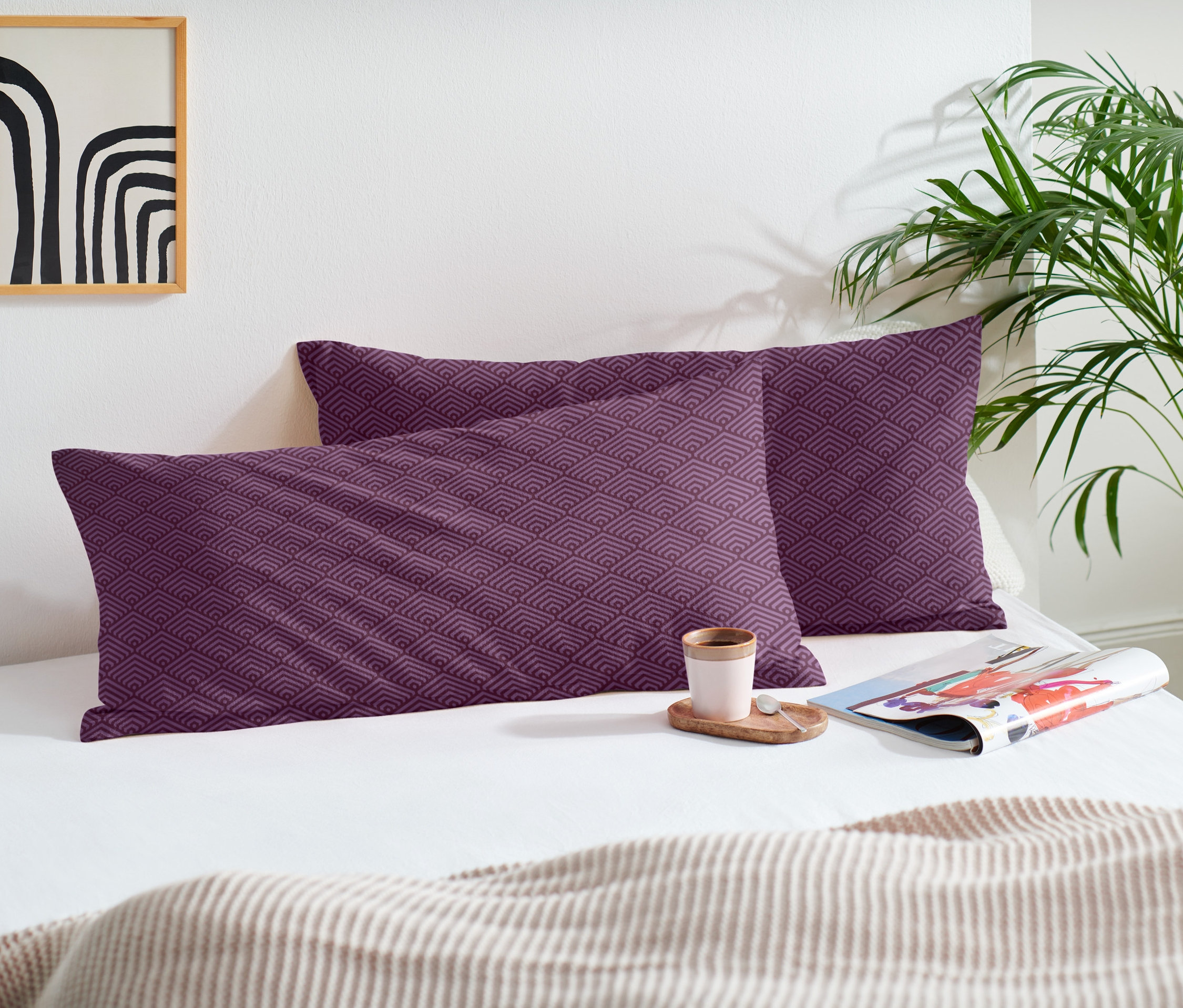 Dve flanelové obliečky na vankúše s fialovým vzorom ležia na posteli so šálkou a časopisom.