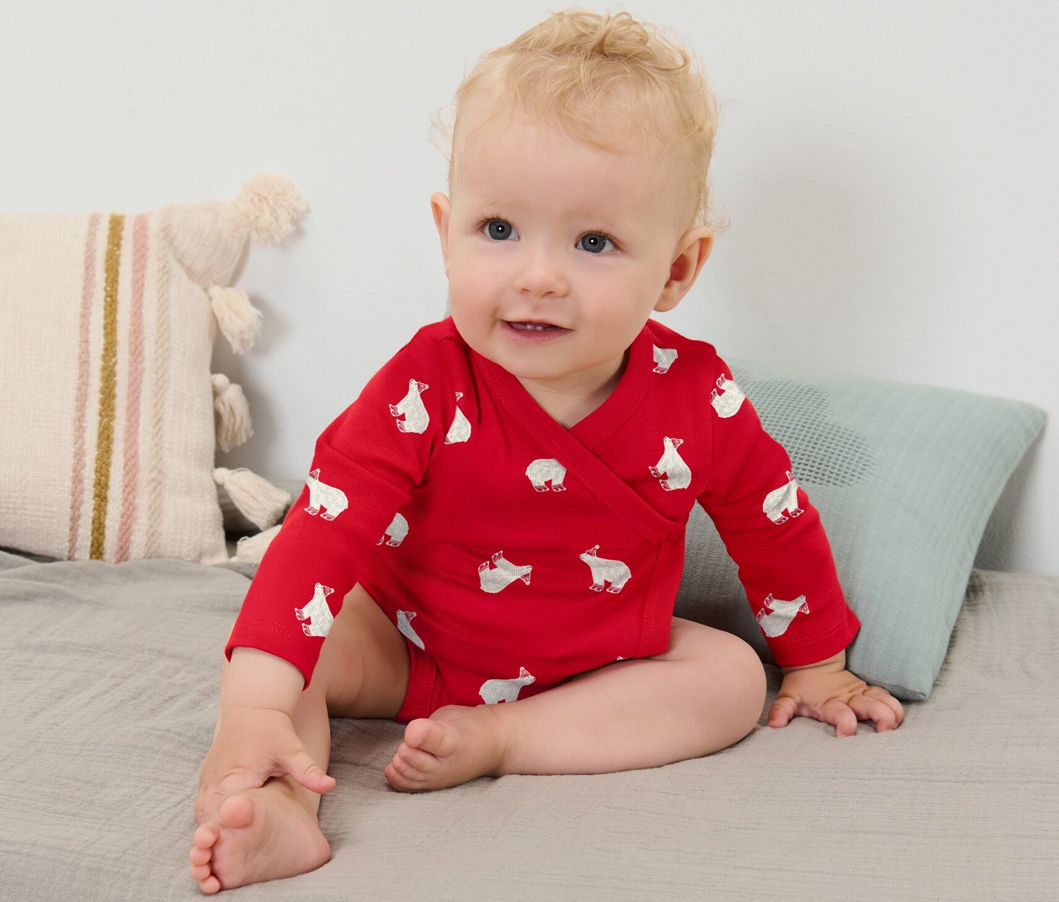 Dievčatko s blond vláskami má na sebe červené body s dlhým rukávom s potlačou ľadových medveďov a sedí na sivej deke.