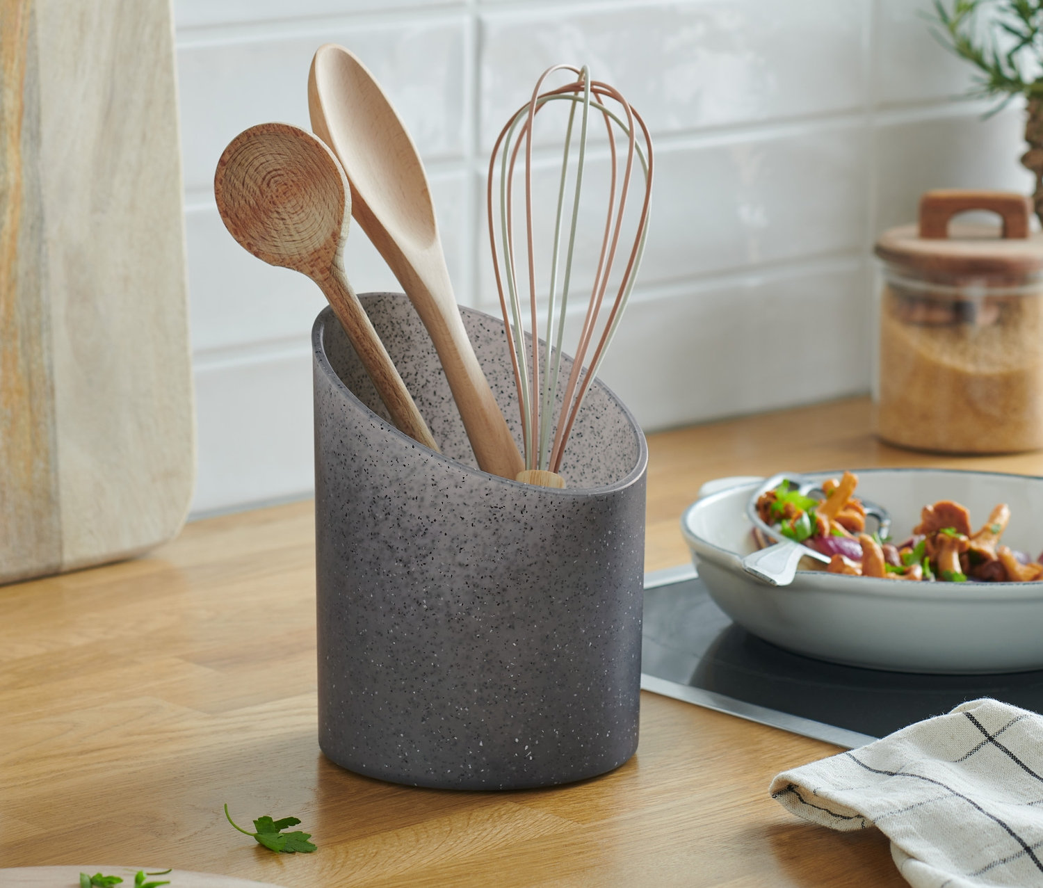 Na kuchynskej linke stojí stojan na kuchynské potreby s granitovým vzhľadom, v ktorom je uložená drevená vareška, lyžica a drôtená metla.