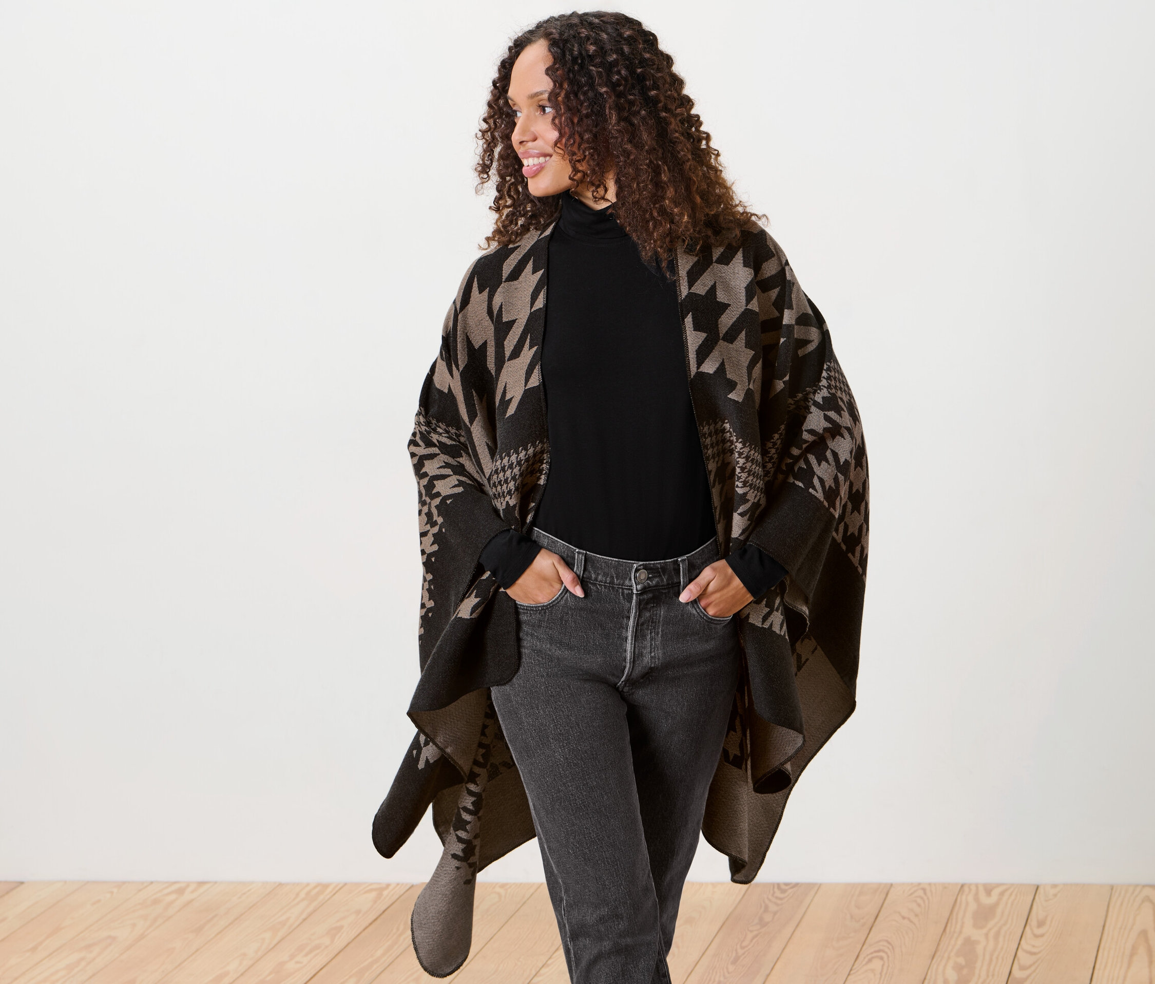 Žena s hnedými kučeravými vlasmi pózuje v ponču.