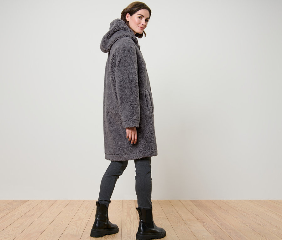 Žena pózuje v sivom plyšovom kabáte s kapucňou.