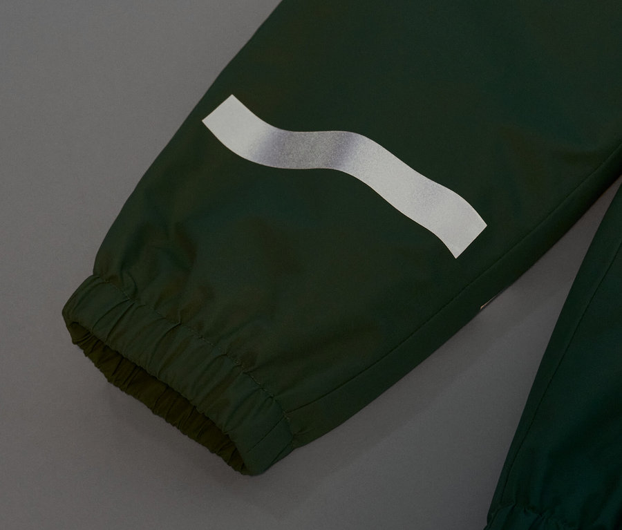 Detail detských nohavíc do dažďa trávovo zelenej farby s reflexným pruhom.
