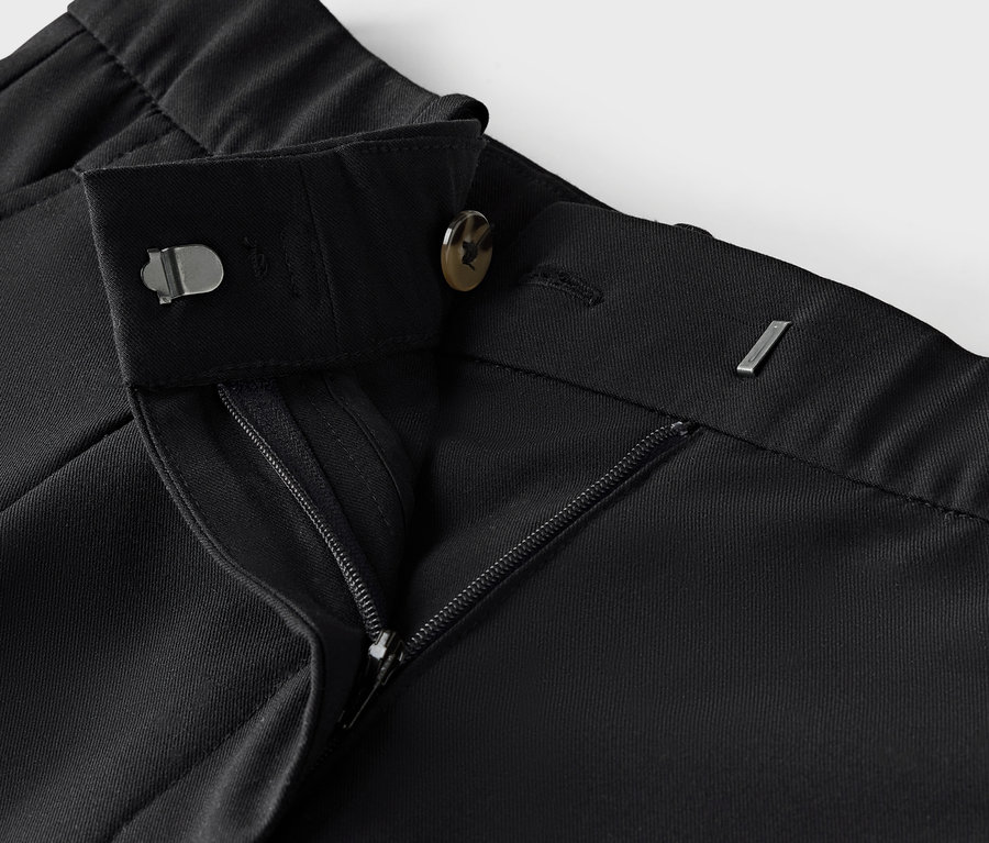 Detail čiernych látkových nohavíc so zipsom a gombíkom.