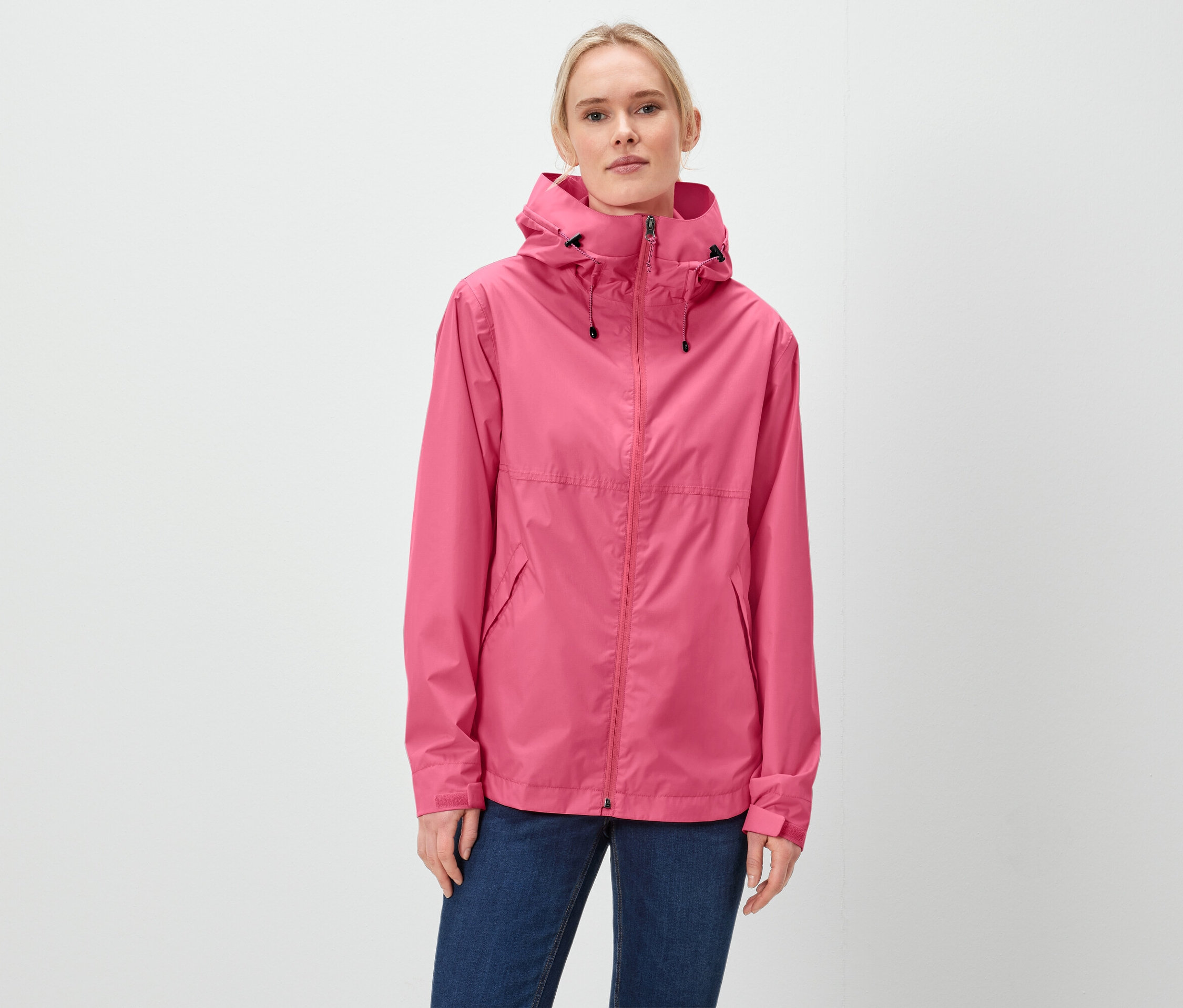 Žena má na sebe ružovú bundu s kapucňou a modré džínsy.