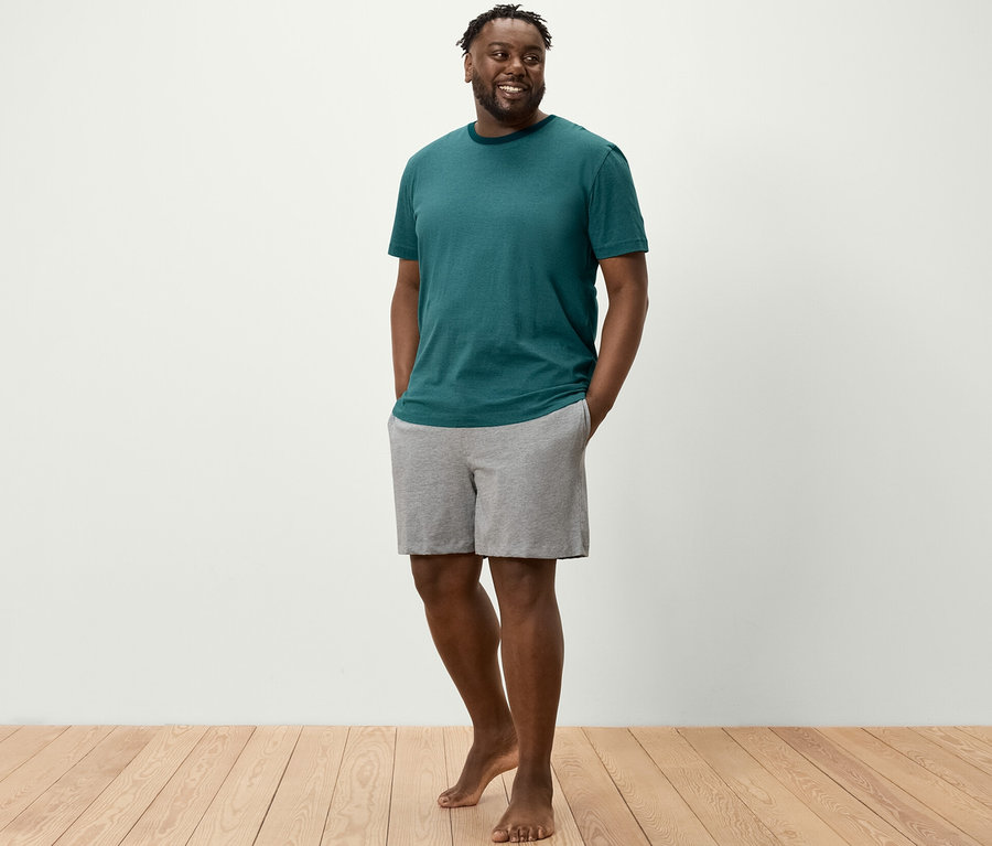 Muž stojí a má ruky vo vreckách šortiek z krátkej pyžamovej súpravy.