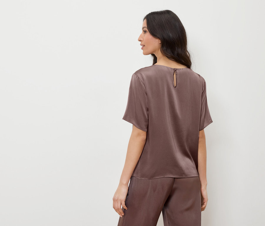 Žena v hnedom saténovom tope a nohaviciach, pozerá sa doľava.