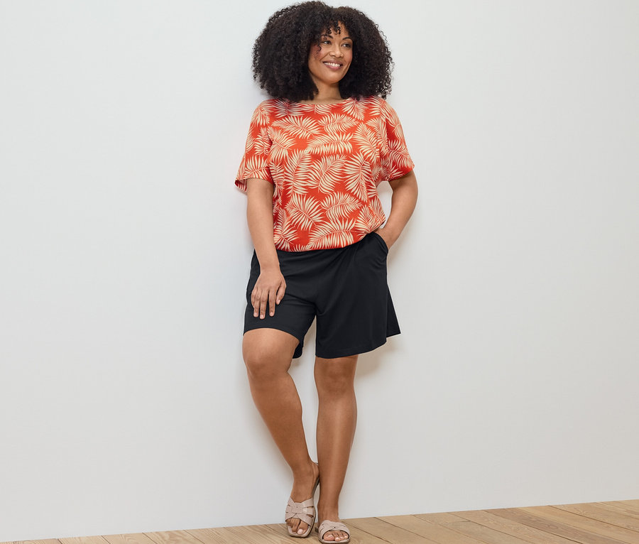 Žena pózuje vo vzorovanom blúzkovom tričku a čiernych džersejových šortkách.