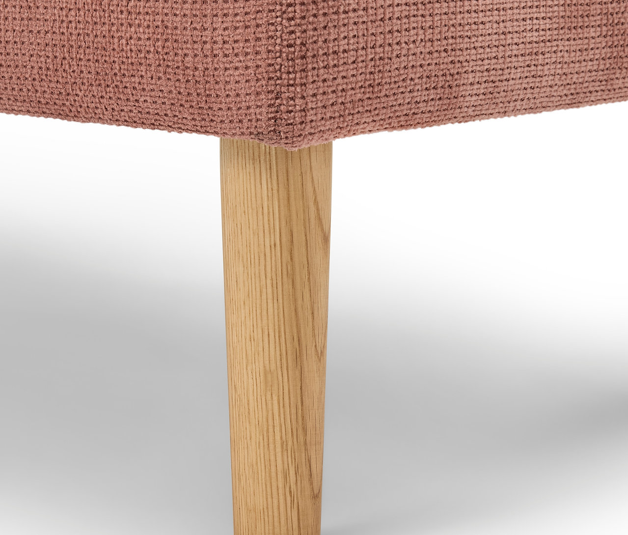 Detail ružového čalúneného nábytku s drevenou nohou.