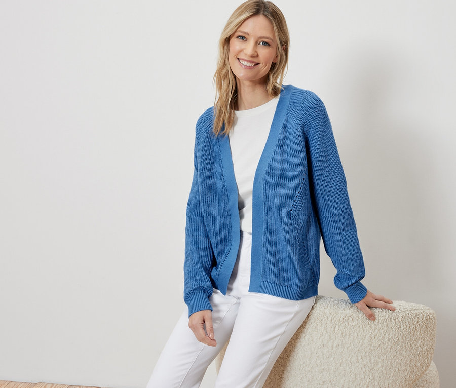 Žena sedí a má na sebe modrý otvorený kardigan.